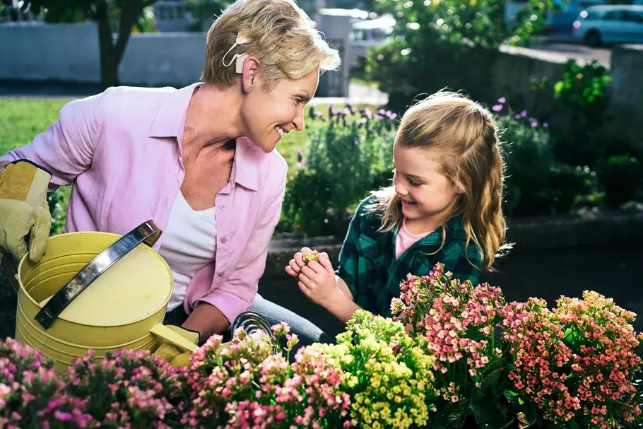 Oma gießt mit ihrer Enkelin den Garten und lächelt sie an.